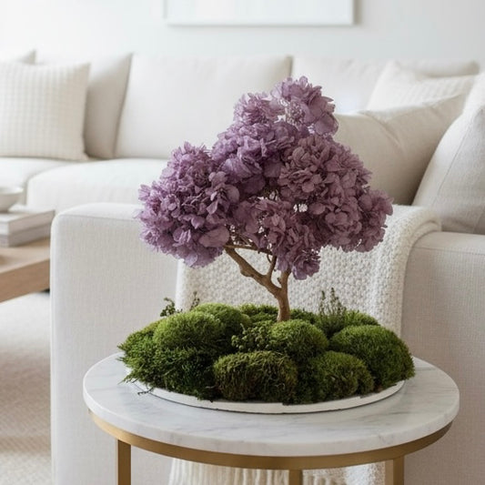 Flowering bonsai zen garden with lavender hydrangea canopy and layered moss landscape on a round white base, styled as Japandi console decor.